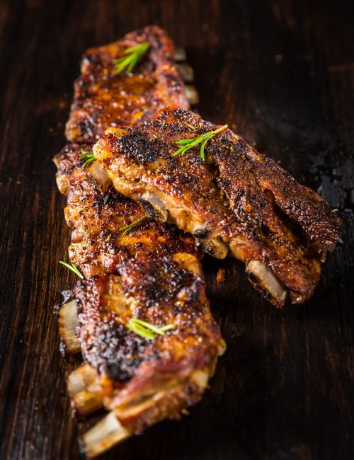 Grilled pork spare ribs with rosemary on wooden background. Barbecue food concept.